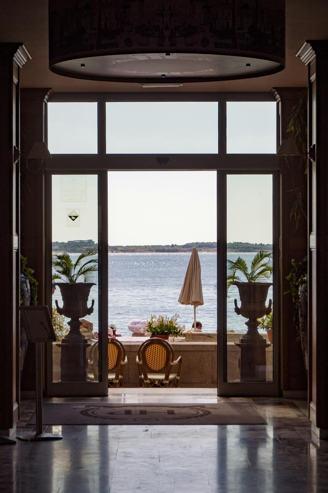 Grande porte-fenêtre ouverte sur la mer, encadrée de vasques et de plantes