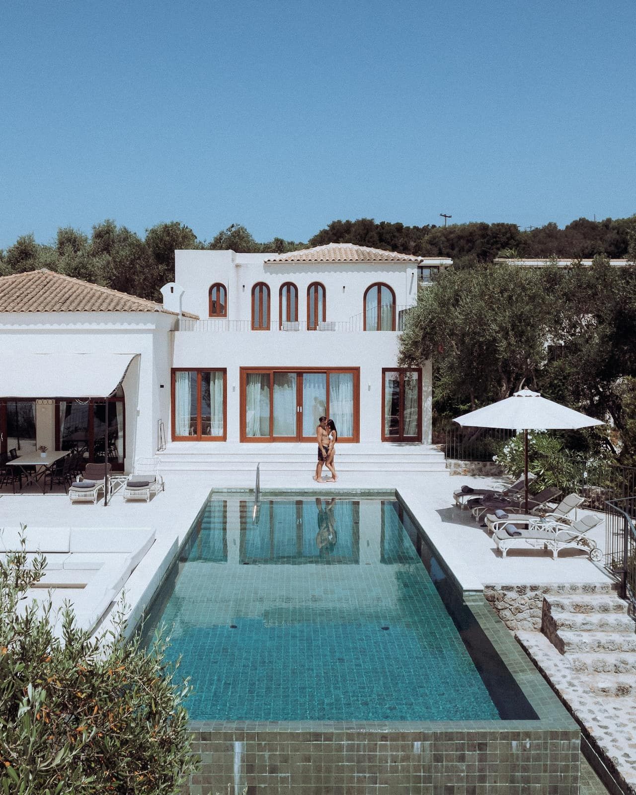 Villa blanche aux fenêtres en arc avec piscine à débordement et terrasse